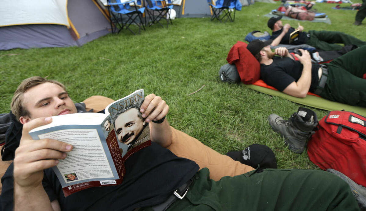 Zach Knudsen, left, reads a book about the life of Albert Einstein as he rests with fellow firefighters from Oregon-based Grayback Forestery at a camp for firefighters battling the Okanogan Complex Fire in Okanogan, Wash., Tuesday, Aug. 25, 2015. The firefighters were resting before their first day fighting fires in Washington state after battling blazes in California for the past three weeks. (AP Photo/Ted S. Warren)