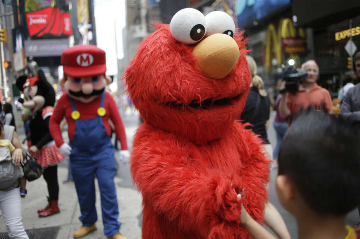 A person dressed as Elmo shakes hands with a pedestrian in Times Square on Monday, July 28, 2014 in New York. New York City Mayor Bill de Blasio said Monday that he believes the people wearing character costumes in Times Square should be licensed and regulated. Dozens of people dressed as kids?’ favorites like Elmo, Cookie Monster and Batman stand near 42nd Street and pose for photos with tourists in exchange for money. De Blasio said the practice has ?“gone too far.?” A man dressed as Spider-man was arrested Saturday, July 28, 2014, after punching a police officer who told him to stop harassing tourists. The City Council is working on legislation that would require the characters to get a city-approved license. (AP Photo/Seth Wenig)