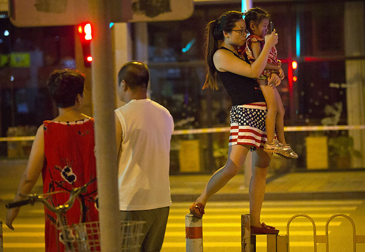A woman holds a child as she stands on a traffic barrier to take a photo of preparations for a military parade in Beijing, Wednesday, Sept. 2, 2015. China will hold a massive military parade in Beijing on Thursday to commemorate the 70th anniversary of Japan's World War II surrender. (AP Photo/Mark Schiefelbein)