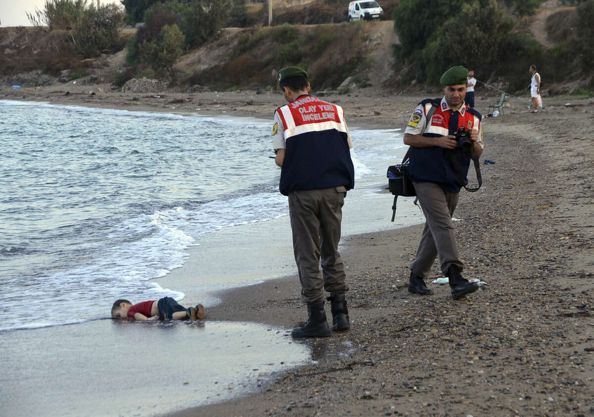 ADDS IDENTIFICATION OF CHILD Paramilitary police officers investigate the scene before carrying the lifeless body of Aylan Kurdi, 3, after a number of migrants died and a smaller number were reported missing after boats carrying them to the Greek island of Kos capsized, near the Turkish resort of Bodrum early Wednesday, Sept. 2, 2015. The family — Abdullah, his wife Rehan and their two boys, 3-year-old Aylan and 5-year-old Galip — embarked on the perilous boat journey only after their bid to move to Canada was rejected. The tides also washed up the bodies of Rehan and Galip on Turkey's Bodrum peninsula Wednesday, Abdullah survived the tragedy. (AP Photo/DHA) TURKEY OUT ONLINE OUT