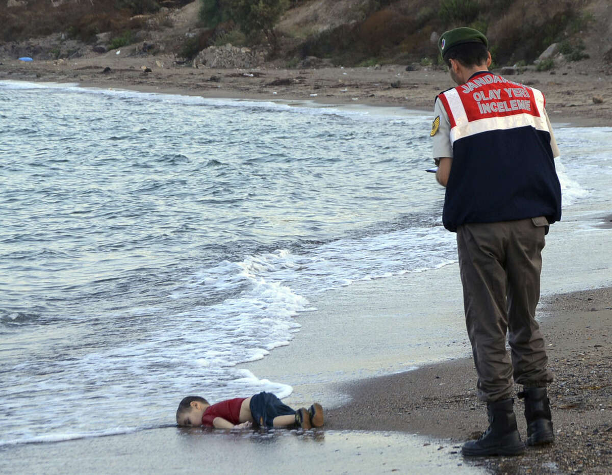 ADDS IDENTIFICATION OF CHILD A paramilitary police officer investigates the scene before carrying the lifeless body of Aylan Kurdi, 3, after a number of migrants died and a smaller number were reported missing after boats carrying them to the Greek island of Kos capsized, near the Turkish resort of Bodrum early Wednesday, Sept. 2, 2015. The family — Abdullah, his wife Rehan and their two boys, 3-year-old Aylan and 5-year-old Galip — embarked on the perilous boat journey only after their bid to move to Canada was rejected. The tides also washed up the bodies of Rehan and Galip on Turkey's Bodrum peninsula Wednesday, Abdullah survived the tragedy. (AP Photo/DHA) TURKEY OUT ONLINE OUT