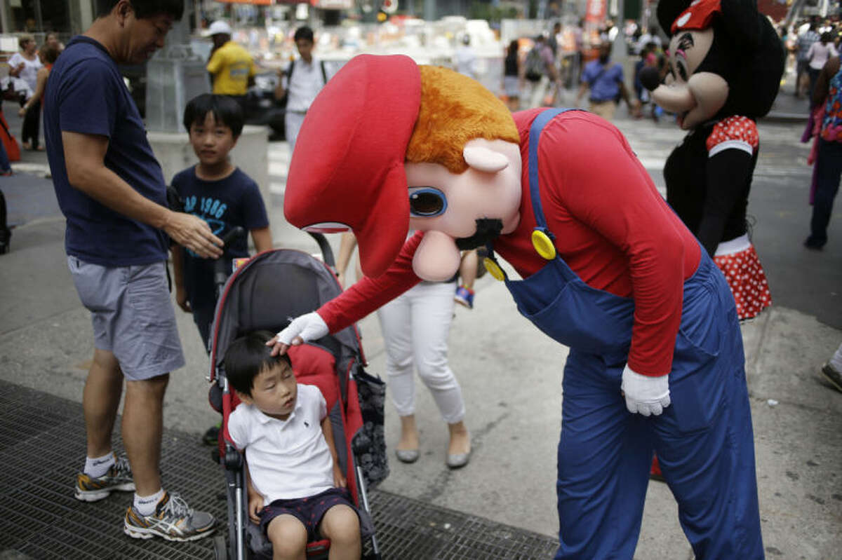 A person dressed as Mario pats a child on the head in Times Square on Monday, July 28, 2014 in New York. New York City Mayor Bill de Blasio said Monday that he believes the people wearing character costumes in Times Square should be licensed and regulated. Dozens of people dressed as kids?’ favorites like Elmo, Cookie Monster and Batman stand near 42nd Street and pose for photos with tourists in exchange for money. De Blasio said the practice has ?“gone too far.?” A man dressed as Spider-man was arrested Saturday, July 28, 2014, after punching a police officer who told him to stop harassing tourists. The City Council is working on legislation that would require the characters to get a city-approved license. (AP Photo/Seth Wenig)