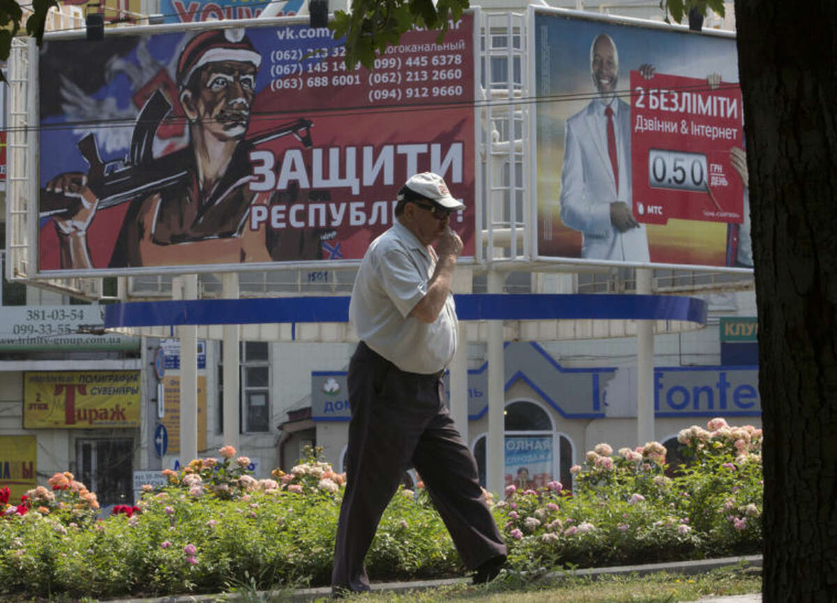 A man walks past a pro-Russian rebels army's agitation poster, left, in the city of Donetsk, eastern Ukraine, Monday, Aug. 4, 2014. The poster reads 'Protect the Republic!'. (AP Photo/Dmitry Lovetsky)