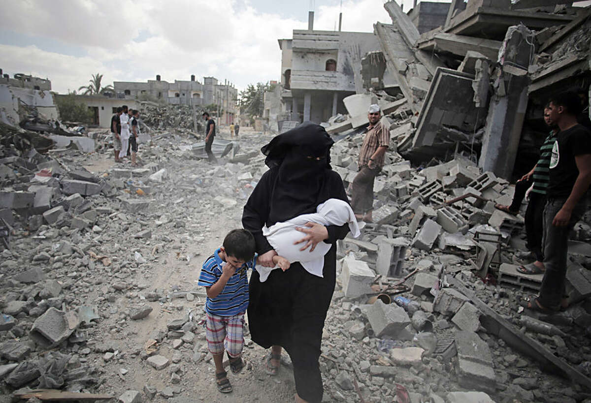 A Palestinian woman passes by rescuers inspecting the rubble of destroyed houses following Israeli strikes in Rafah refugee camp, southern Gaza Strip, Monday, Aug. 4, 2014. (AP Photo/Khalil Hamra)