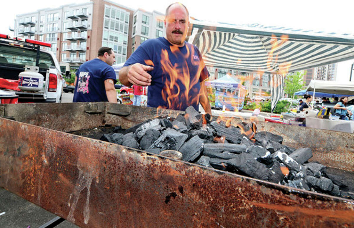 Hour photo / Erik Trautmann Firefighter Pete Cogliano of the Belltown Fire Department fires up the grill at Saturday's barbecue showdown at Fairway Market in Stamford.