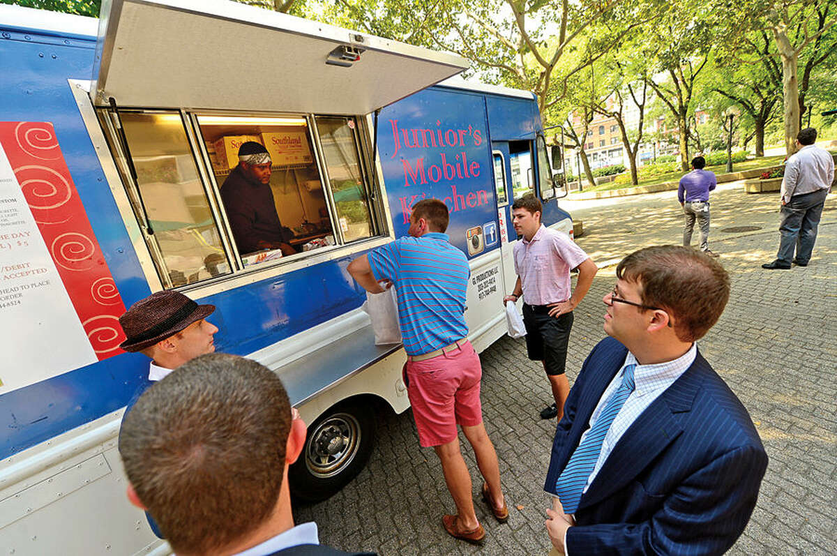 Hour photo / Erik Trautmann Customers line up for cuisine from Junior's Mobile Kitchen at Veteran's Park in downtown Stamford Wednesday. Stamford officials will be cracking down on the food trucks, which routinely park at the park.