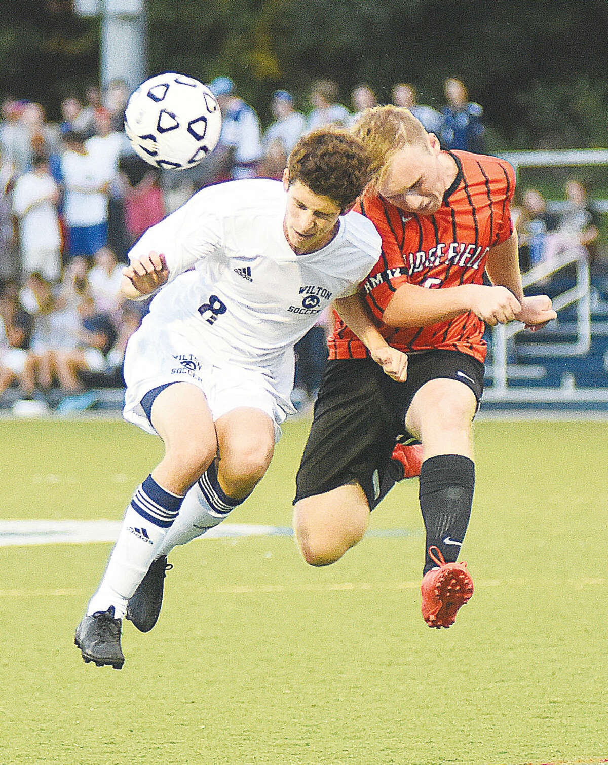 Hour photo/John Nash - Jordan Lord, left, heads the ball against Ridgefield Tigers player Edwin Hassenstein during Monday's FCIAC boys soccer game in Wilton.