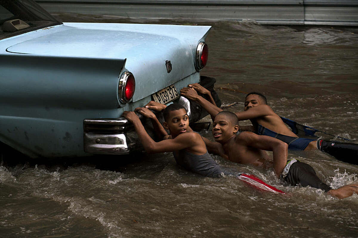 Youths hang from the rear bumper of a vintage American car as they play in a flooded street, after a heavy rain in Havana, Cuba, Wednesday, Oct. 14, 2015. (AP Photo/Ramon Espinosa)