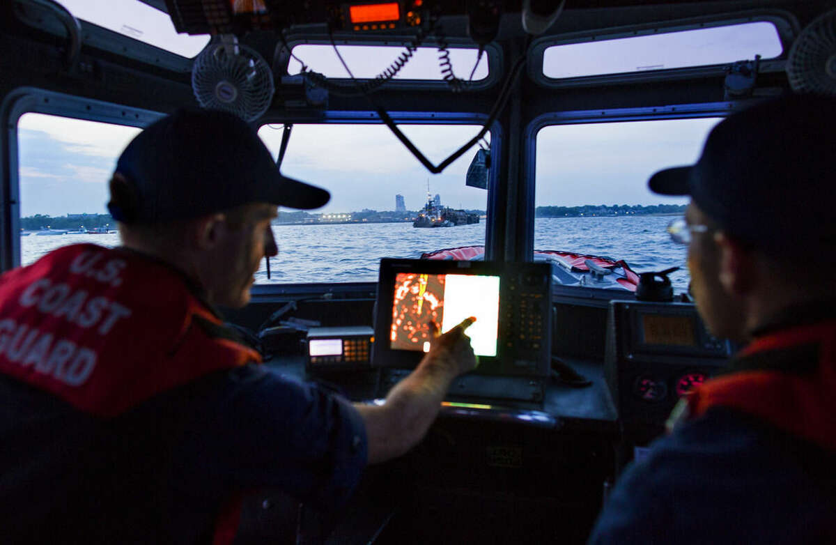 In this photo taken July 12, 2014, U.S. Coast Guard 2nd Class Petty Officer Geoffrey Burns, left, and 3rd Class Petty Officer John Huber, at the wheel of a response boat, patrol near a barge, seen in front window, that would soon be the water base of a fireworks display off Glen Island in western Long Island Sound near New Rochelle, N.Y. A wedding celebrated on Glen Island featured fireworks, and the Coast Guard engaged in keeping a safe zone for boaters around the pyrotechnics. (AP Photo/Craig Ruttle)