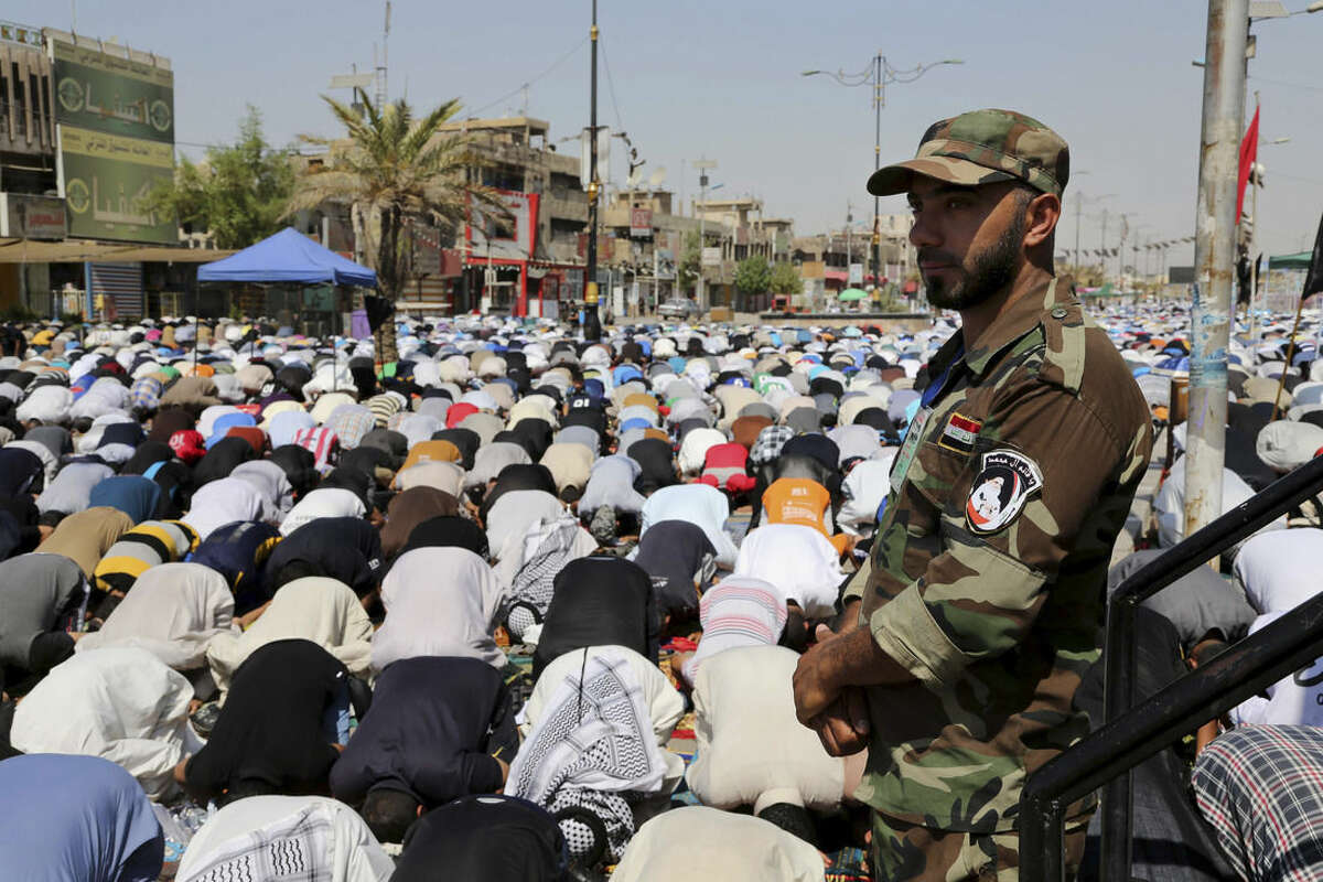 A Shiite fighter stands guard over followers of Shiite cleric Muqtada al-Sadr attending open-air Friday prayers in the Shiite stronghold of Sadr City, Baghdad, Iraq, Friday, Sept. 5, 2014. (AP Photo/Karim Kadim)