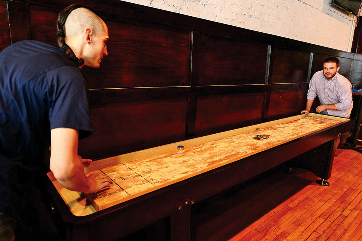 Hour photo / Erik Trautmann Owners, Matt Bacco, Casey Dohme play shuffleboard wwhich will be a featured game at the new sports bar, Blind Rhino, on North Main St in SoNo next Friday