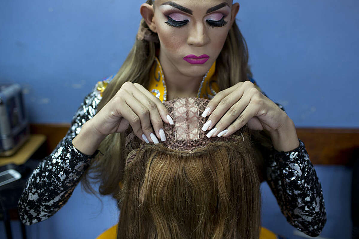In this Oct. 18, 2015 photo, contestant Jorge Solano, Miss Gay Cojedes, inspects his wig backstage at the ninth annual Miss Gay Venezuela beauty pageant in Caracas, Venezuela. Some contestants can afford to use wigs made of real, natural hair, while others use synthetic wigs. (AP Photo/Ariana Cubillos)