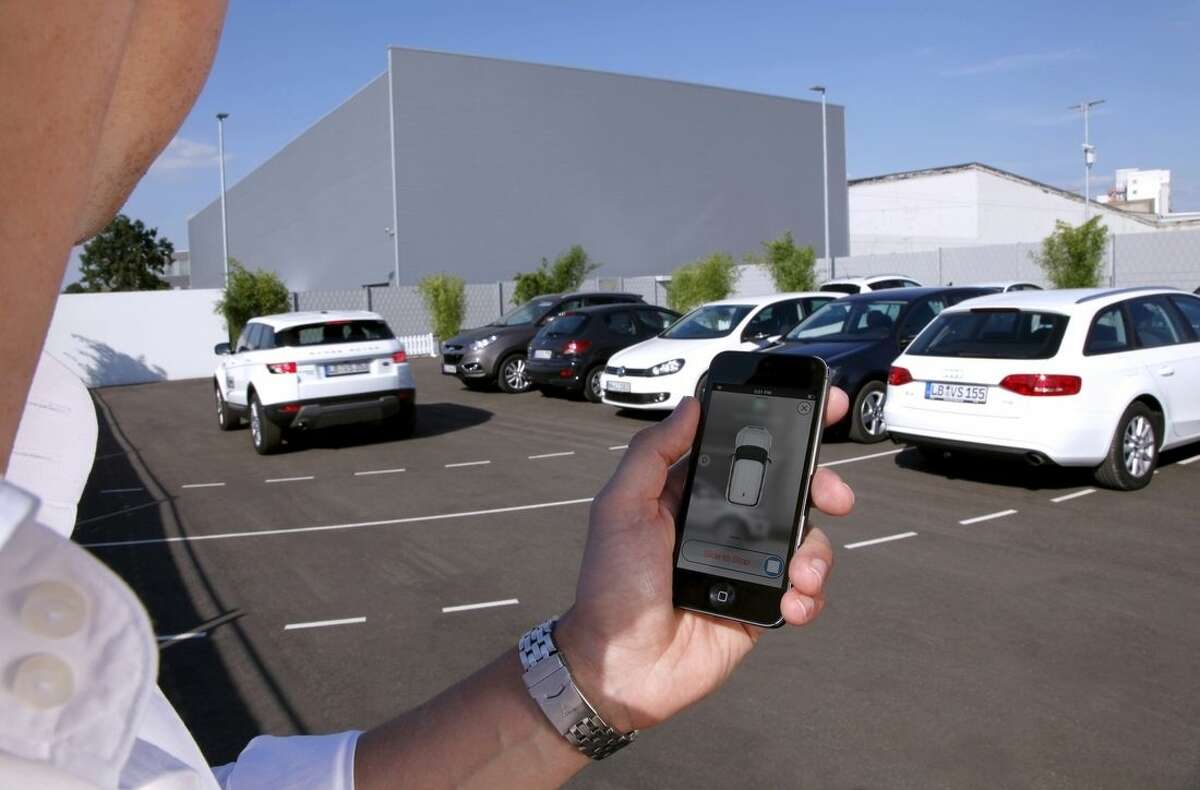 In this undated photo supplied by Valeo, a person activates a self-parking vehicle via a smartphone application. Technology being honed by the French auto parts maker uses a dozen ultrasonic sound-wave sensors, 360-degree cameras and a laser scanner to allow a vehicle to safely park within a few centimeters of other vehicles. (AP Photo/Valeo)