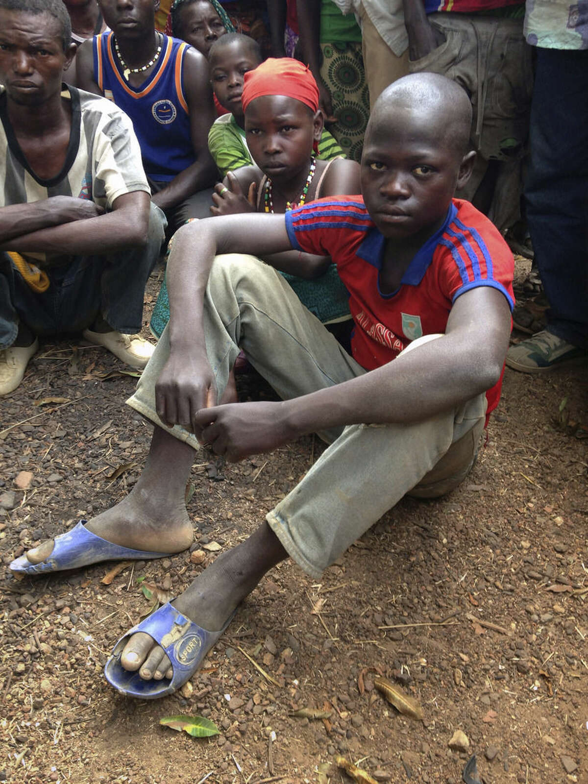 In this Feb. 27, 2014, photo, survivor Maximin Lassananyant, 13, sits with his father and other relatives in the village of Nzakoun, Central African Republic. Lassananyant said that he ran for his life the night Muslim rebels attacked the village of Nzakoun on Feb. 3. His mother, brother and sister were among the 23 dead while he survived by hiding in the countryside until the rebels left. His father, looks on at left. (AP Photo/Krista Larson)
