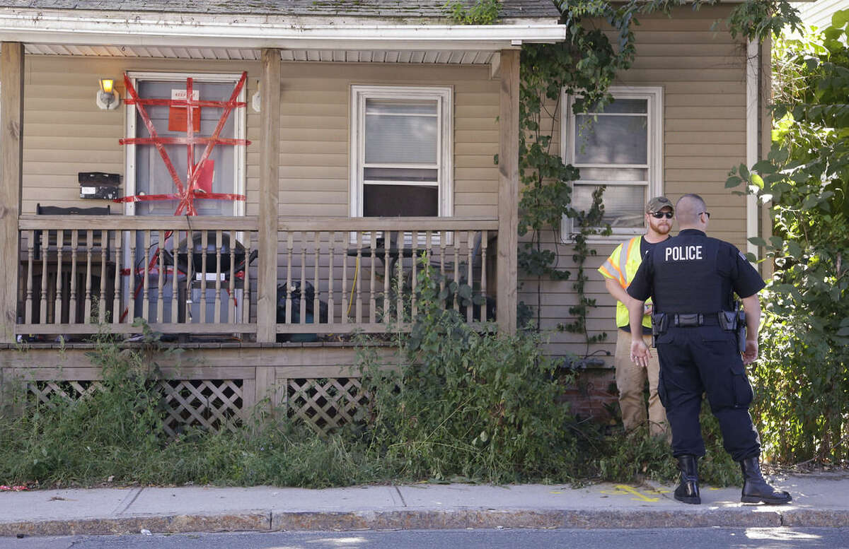 A Blackstone police officer talks with a utility worker while standing post outside a house where a Massachusetts prosecutor said the bodies of three infants were found Thursday in Blackstone, Mass., Friday, Sept. 12, 2014. Both "condemned" and "keep out" signs are attached behind police tape to the front door. The utility worker laid some paint markings on the street in front of the house. (AP Photo/Stephan Savoia)