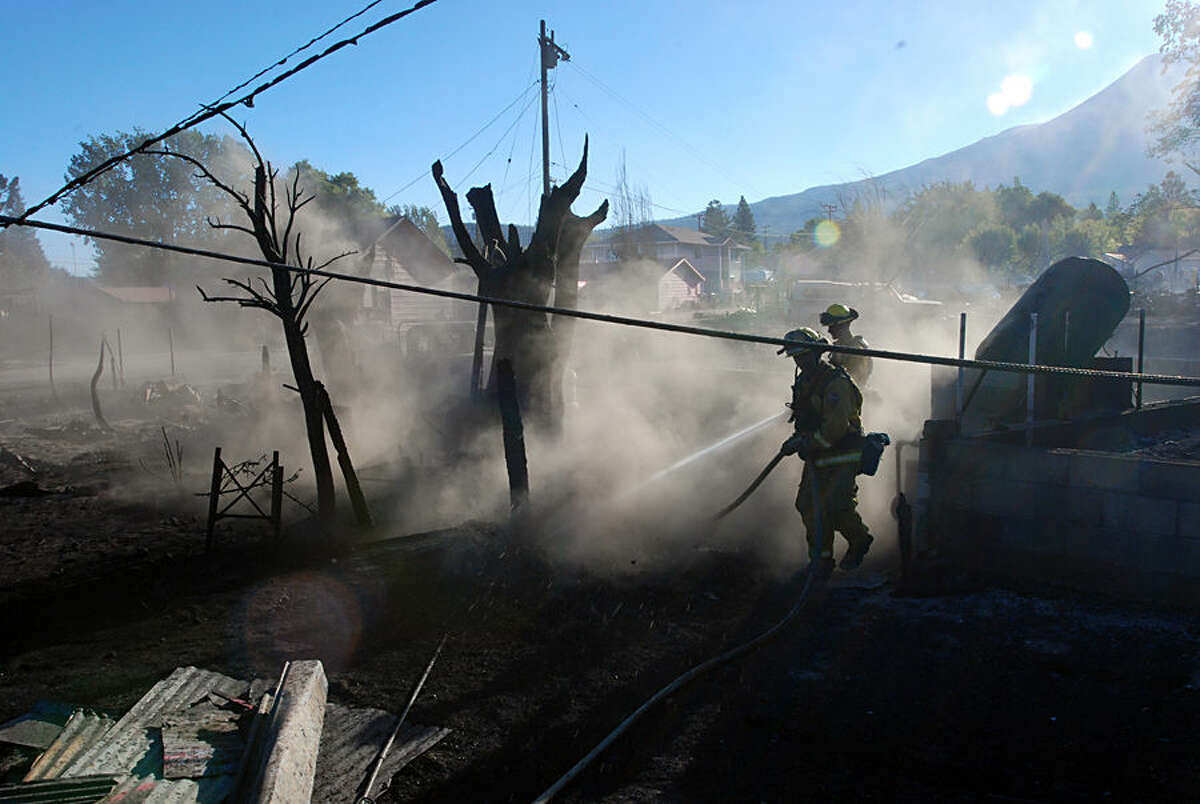 Firefighters hose down the smoldering remains of a home, Tuesday, Sept. 16, 2014, in Weed, Calif. A fast-moving wildfire destroyed at least 100 structures before winds died down and firefighters got a line around most of the fire. (AP Photo/Jeff Barnard)