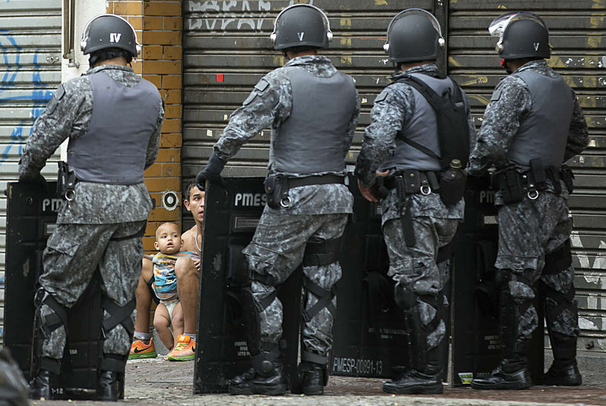A man and a baby, who voluntarily left an occupied building, are framed by the shields of police standing guard during an eviction operation, in downtown Sao Paulo, Brazil, Tuesday, Sept. 16, 2014. The eviction of 200 families from the building led to violent clashes. Protesters set at least one bus ablaze while police fired rubber bullets, tear gas and stun grenades in an effort to disperse the crowd. (AP Photo/Andre Penner)