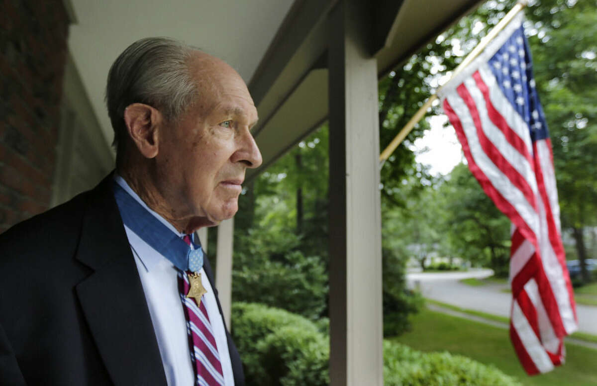 FILE - In this Friday, July 12, 2013, file photo, retired U.S. Navy Capt. Thomas Hudner, who was awarded the Medal of Honor by President Truman, poses on the porch at his home in Concord, Mass. Hudner’s lifelong quest to recover the remains of his trusted wingman Ensign Jesse Brown, the U.S. Navy’s first black combat pilot, whose plane was shot down over North Korea in December 1950, is told in a new book titled “Devotion” by author Adam Makos. (AP Photo/Charles Krupa, File)