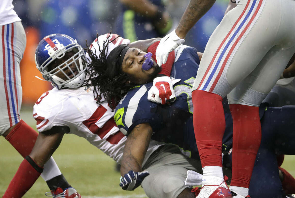 Seattle Seahawks' Marshawn Lynch is tackled by New York Giants middle linebacker Jameel McClain, left, after losing his helmet in the second half of an NFL football game, Sunday, Nov. 9, 2014, in Seattle. The Seahawks beat the Giants, 38-17. (AP Photo/Scott Eklund)