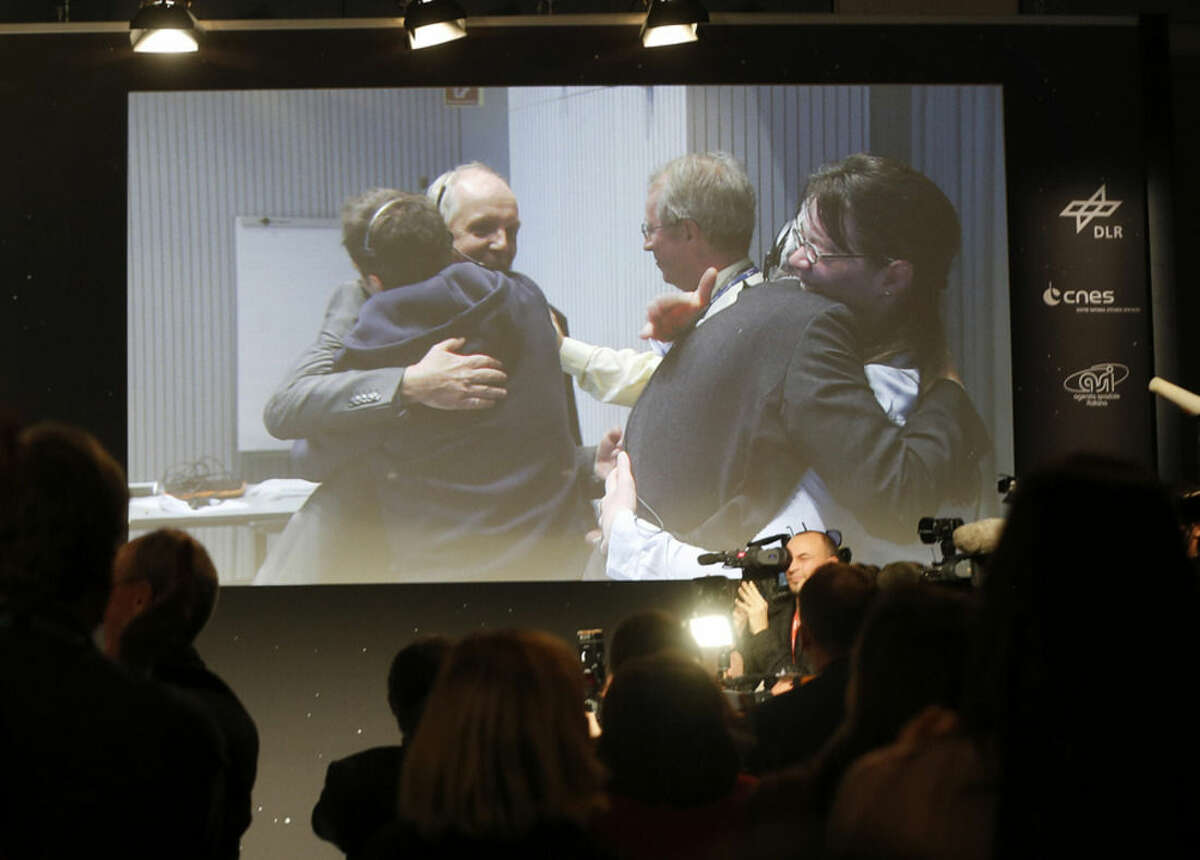 Celebrating scientists in the main control room appear on a video screen at the European Space Agency after the first unmanned spacecraft Philae landed on a comet called 67P/Churyumov-Gerasimenko, in Darmstadt, Germany, Wednesday, Nov. 12, 2014. Europe's Rosetta space probe was launched in 2004 with the aim of studying the comet and learning more about the origins of the universe. (AP Photo/Michael Probst)