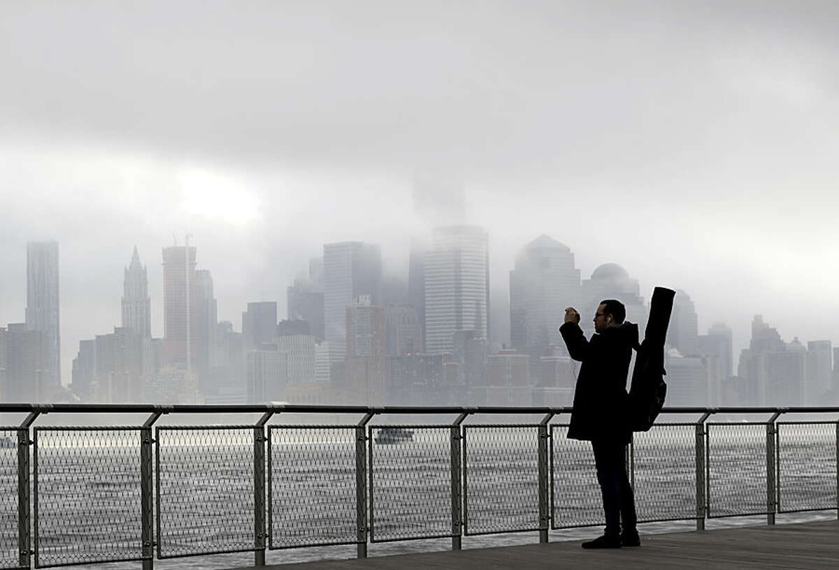 Richard Espinal, of New York City, pauses during his walk to work as a music instructor to photograph the fog blanketing New York City, Wednesday, Nov. 12, 2014, from the Hudson River front in Hoboken, N.J. The National Weather Service said the fog reduced visibility to a quarter mile or less. Motorists were advised to slow down. (AP Photo/Julio Cortez)