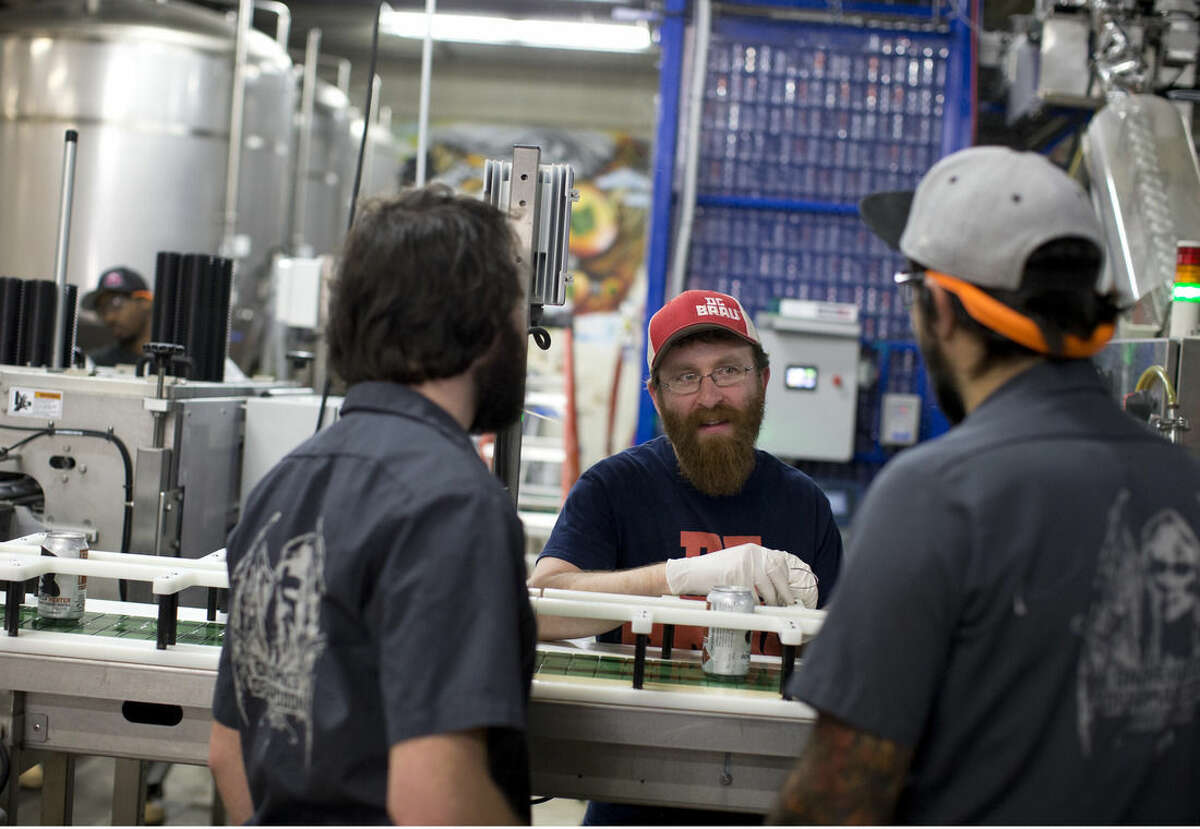 In this Wednesday, Nov. 12, 2014 photo, DC Brau Brewing Co. employees, from left, Jake Agger, Jason Budman, and Chad Hooper, talk in the the canning area at the brewery in Washington, D.C. The district's small business health insurance exchange helped DC Brau offer more than 50 insurance options to its employees starting in September. That’s a massive leap from the two choices it usually cobbled together. (AP Photo/Carolyn Kaster)