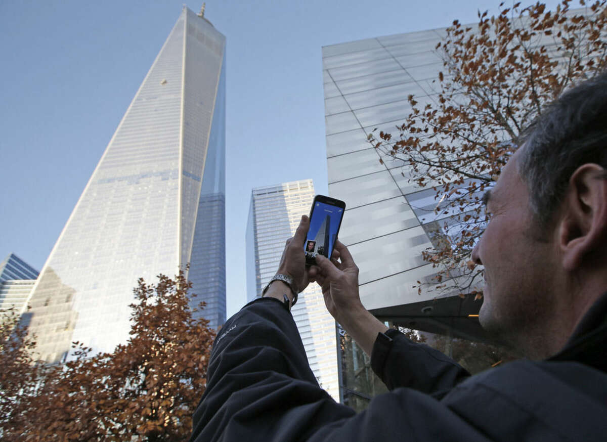 Tomas Vruns, from Muenster, Germany, uses his cell phone to take a picture of 1 World Trade Center where a scaffolding still dangled hours after two window washers were rescued by firefighters who sawed through a window to reach them, Wednesday, Nov. 12, 2014, in New York. The accident, which officials said was caused by a malfunctioning cable, happened little more than a week after workers began moving into the nation's tallest building. (AP Photo/Kathy Willens)
