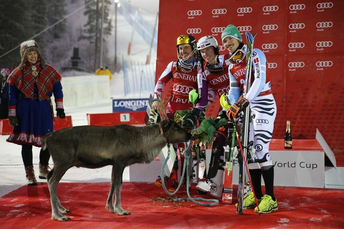 Henrik Kristoffersen, center, winner of an alpine ski, men's World Cup slalom race, flanked by second placed Marcel Hirscher, left, and third placed Felix Neureuther, poses next to a reindeer in Levi, Finland, Sunday, Nov. 16, 2014. (AP Photo/Giovanni Auletta)