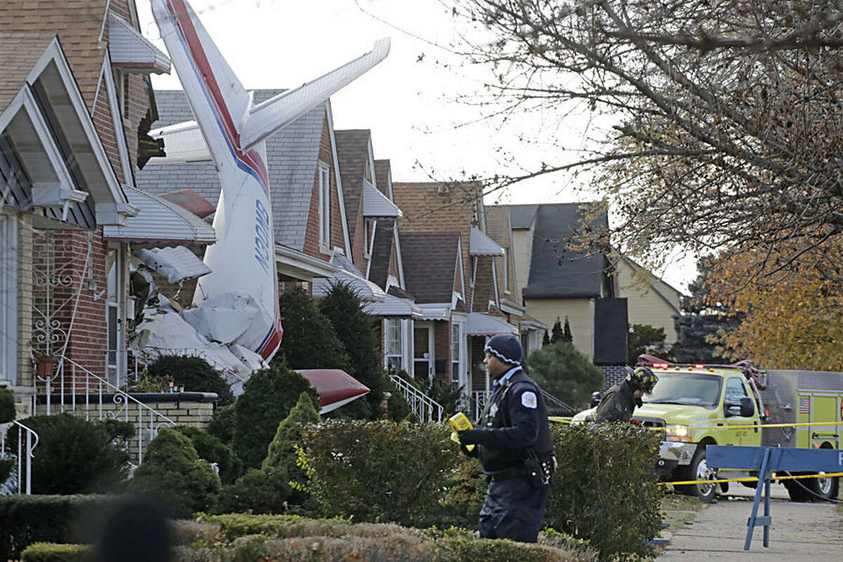 Police and fire officials walk near a small twin-engine cargo plane that crashed into a home on Chicago's southwest side early Tuesday, Nov. 18, 2014. The Aero Commander 500 that had taken off from Midway International Airport slammed into the front of the home and plunged into the basement. Fire Department spokesman Larry Langford says two occupants of the home were unhurt. The pilot was killed in the crash. (AP Photo/M. Spencer Green)
