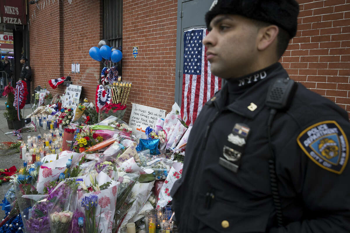 A New York Police Department officer stands guard beside a makeshift memorial, Monday, Dec. 22, 2014, near the site where officers Rafael Ramos and Wenjian Liu were murdered in the Brooklyn borough of New York. Police say Ismaaiyl Brinsley ambushed the two officers in their patrol car in broad daylight Saturday, fatally shooting them before killing himself inside a subway station. (AP Photo/Seth Wenig)