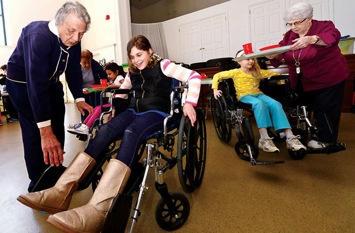 Hour photo / Erik Trautmann Barbra Dunlap helps 4th grader Brenna Dominick into a wheelchair as students from Marvin Elementary School visit The Marvin senior residence and experience what it is like to have disabilities related to aging. During the annual event students rotate through several "stations" managed by senior residents of The Marvin and they experience some of the physical and sensory challenges of aging.