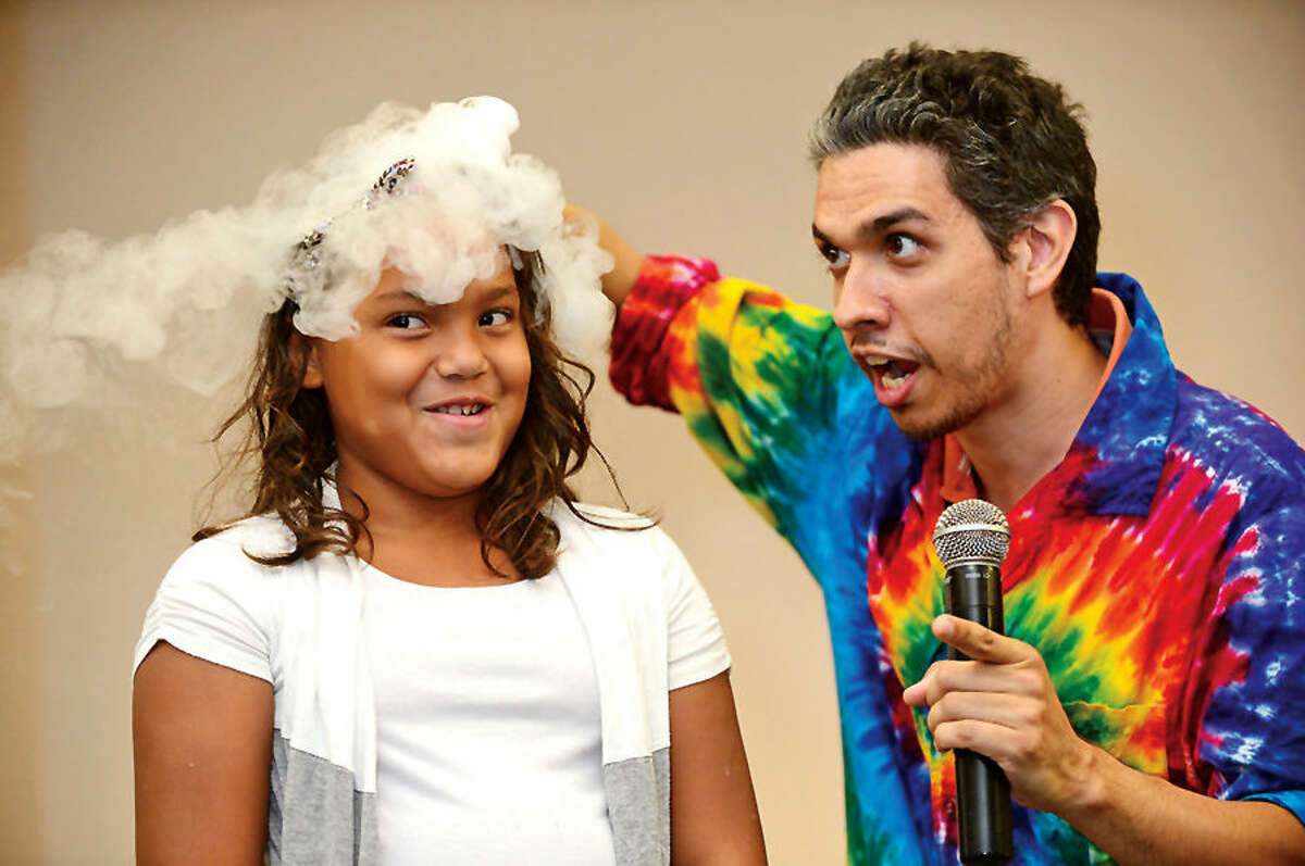 Hour photo / Erik Trautmann Interactive science storyteller, Justin Maruri, otherwise known as a Scienceteller, and volunteer Camila Santos use dry ice during the presentation of “Dragons & Dreams!” at the South Norwalk Branch Public Library Thursday. The Sciencetellers teach science to their audience by telling a lively, interactive and exciting story intertwined with basic science principles.