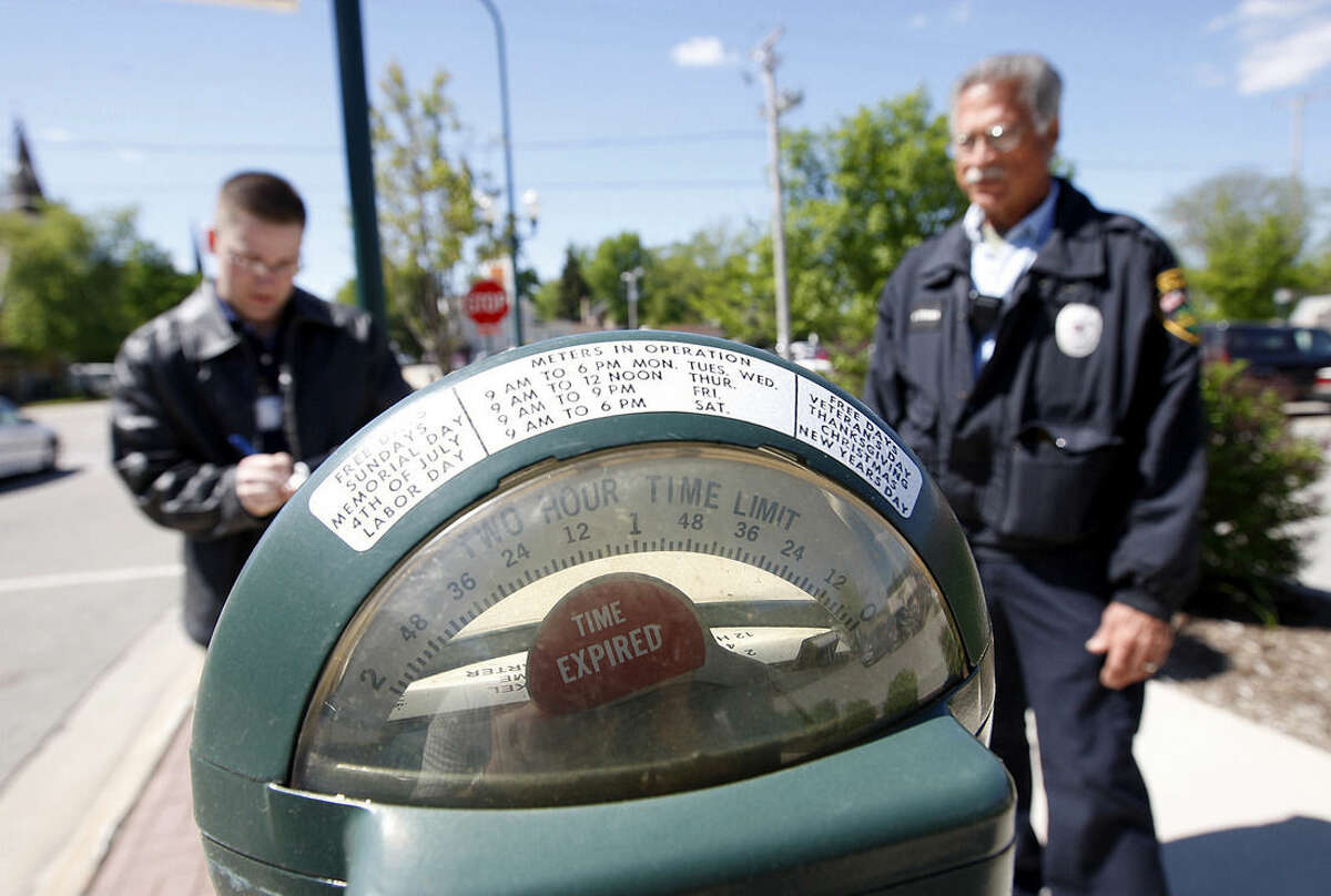 In this May 21, 2008 photo, parking enforcement officer Giovanni Serra, left, watches as Sycamore Police Department intern Justin Keller writes a ticket in downtown Sycamore, Ill. Sycamore is one of the last communities in the country with parking meters that accept pennies. A few other towns have hung onto maybe a dozen or so meters as a reminder of a simpler time. But people who track parking in the United States say they’ve never heard of another town that has anywhere close to the 316 that are in Sycamore. (AP Photo/Daily Chronicle, Eric Sumberg) MANDATORY CREDIT