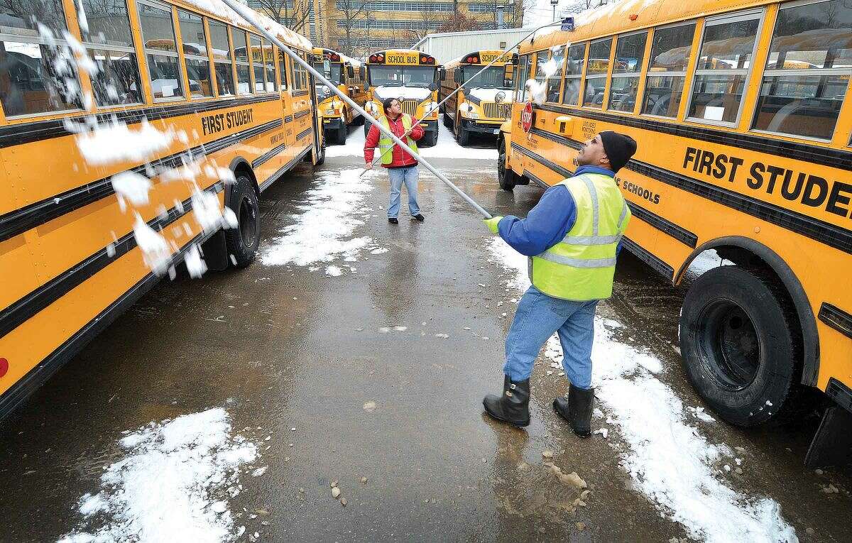 Hour Photo/Alex von Kleydorff Drivers Daniel Davis and Marco Flores use roof rakes to clear snow from the tops of school buses at First Student bus depot in Norwalk. Norwalk Public school is back in session on Wednesday and the more than 60 busses need to be made safe for sudents.