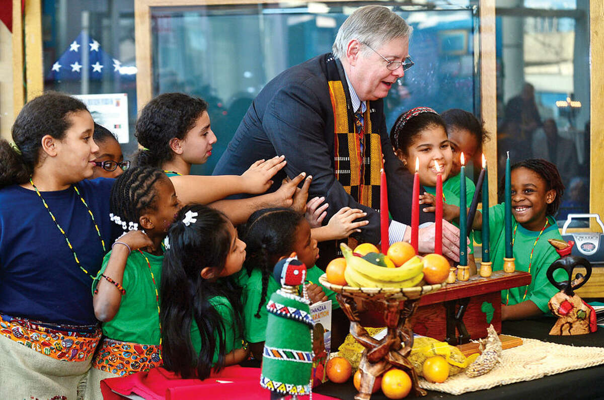 Hour photo / Erik Trautmann Stamford Mayor David Martin lights candles with children from the community during the city’s 20th annual Kwanzaa celebration Tuesday at the Stamford Government Center.