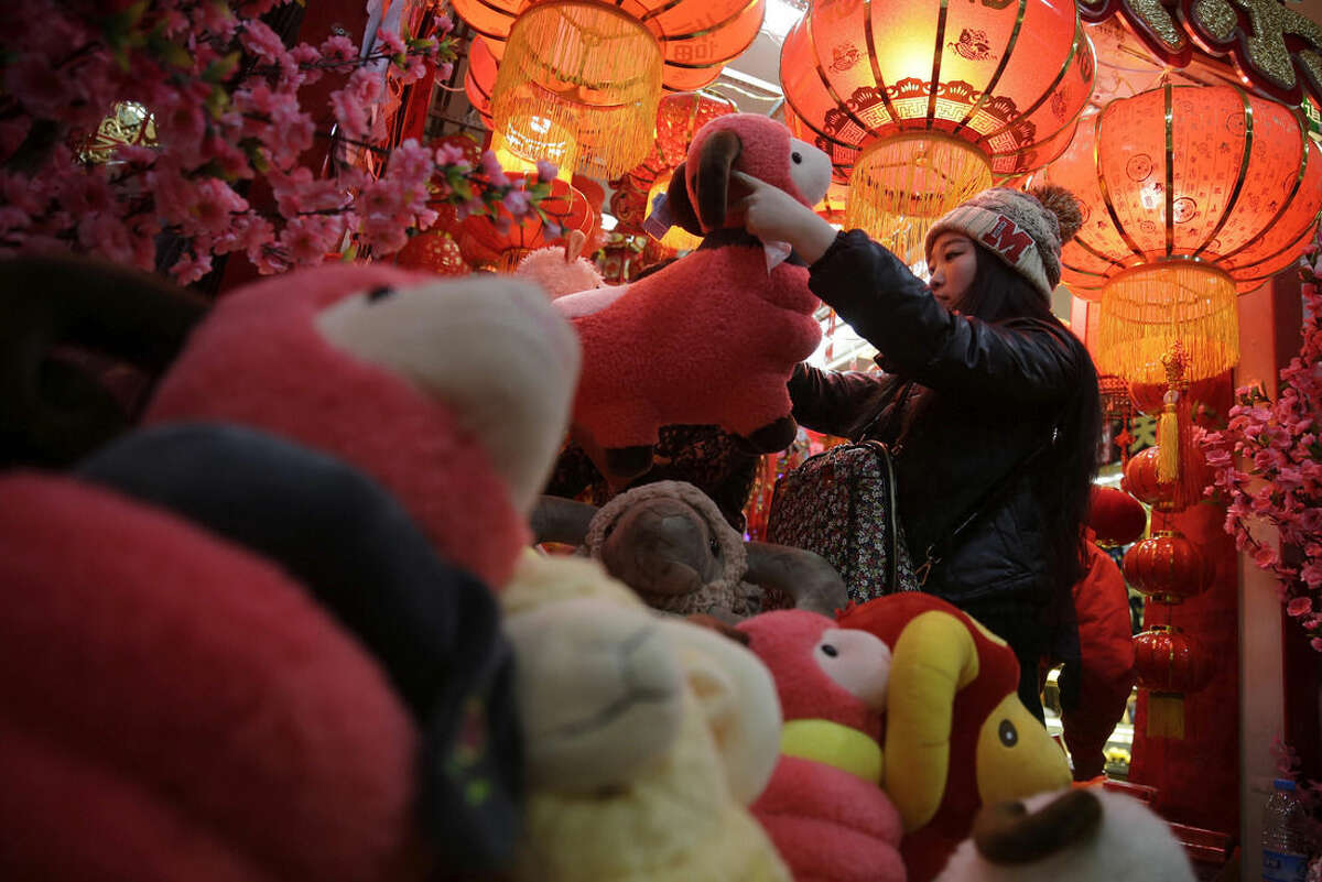 In this Feb. 12, 2015 photo, a woman shops toy sheep for Lunar New Year decorations in Beijing, China. Chinese were seeing in the Year of the Sheep on Thursday, Feb. 19 but with fortune-tellers predicting accidents and an unstable economy and some parents-to-be fretting over the year’s reputation for docile kids, it wasn’t exactly warming everyone’s heart.(AP Photo/Andy Wong)