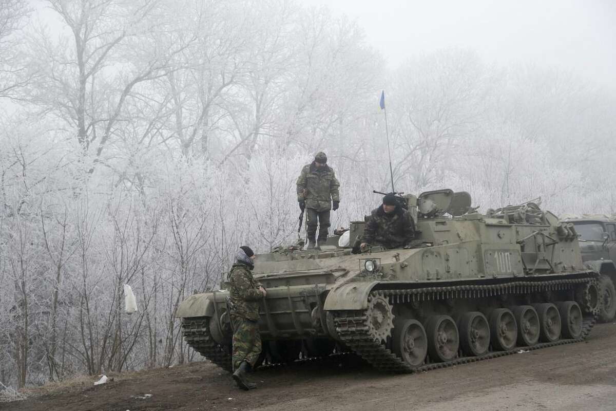 Ukrainian government soldiers rest by armored vehicle on the road between the towns of Dabeltseve and Artemivsk, Ukraine, Sunday, Feb. 15, 2015. International attention will be focused in the coming days on the strategic railway hub of Debaltseve, where Ukrainian government forces have for weeks been fending off severe onslaughts from pro-Russian separatists. A cease-fire was declared in eastern Ukraine, kindling slender hopes of a reprieve from a conflict that has claimed more than 5,300 lives. (AP Photo/Petr David Josek)