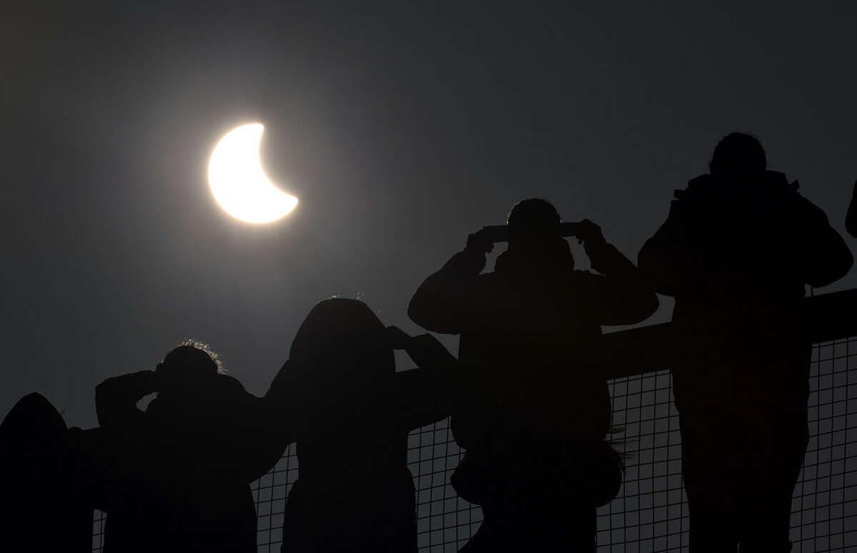 People watch as a solar eclipse begins over the Eden Project near St Austell in Cornwall, England Friday March 20, 2015. An eclipse is darkening parts of Europe on Friday in a rare solar event that won't be repeated for more than a decade. (AP Photo/PA, Ben Birchall) UNITED KINGDOM OUT: NO SALES: NO ARCHIVE:
