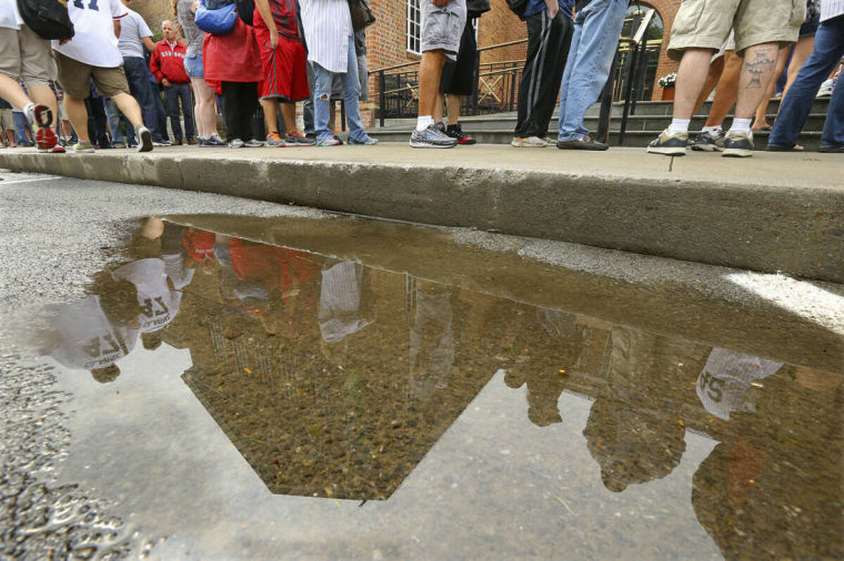 Hundreds of baseball fans are reflected in a puddle of rain water along with the building as they line up outside the National Baseball Hall of Fame despite the weather on Sunday, July 27, 2014, in Cooperstown. The annual Hall of Fame Induction Ceremony will take place nearby at the Clarks Sports Center. (AP Photo/Atlanta Journal-Constitution, Curtis Compton) MARIETTA DAILY OUT; GWINNETT DAILY POST OUT; LOCAL TELEVISION OUT; WXIA-TV OUT; WGCL-TV OUT