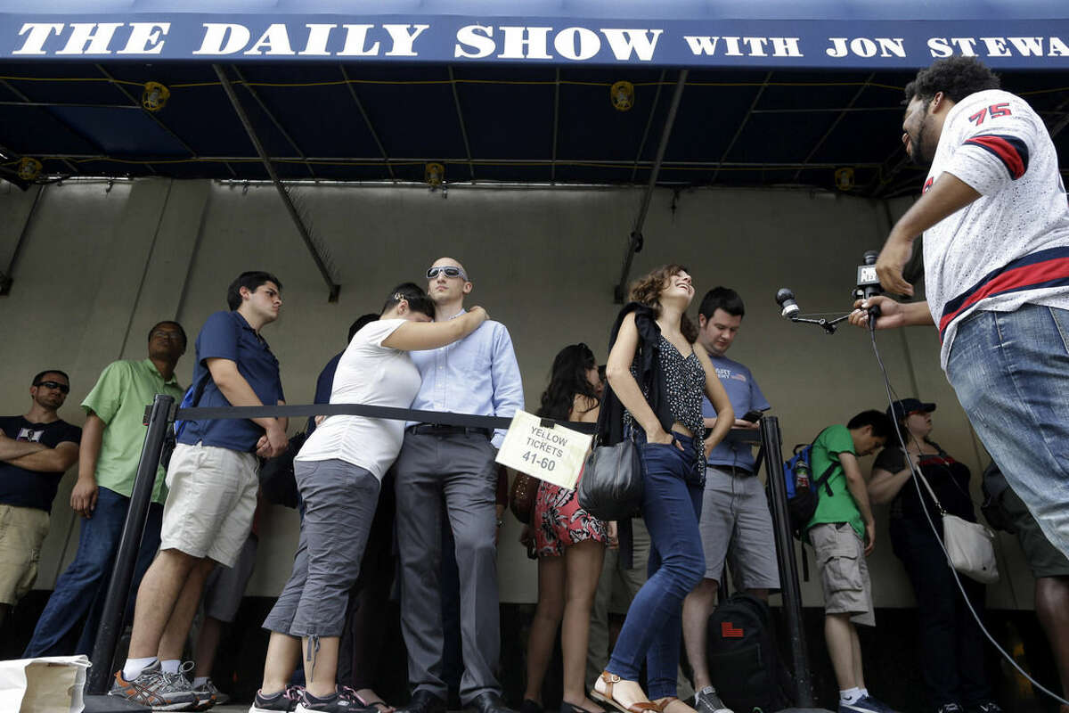 Alexandra Mele, second from right, is interviewed and Ariana and Isaac Levin, embrace as they wait in line to enter for the final taping of "The Daily Show with Jon Stewart," Thursday, Aug. 6, 2015, in New York. Stewart says goodbye on Thursday, after 16 years on the show that established him as America's foremost satirist of politicians and the media. (AP Photo/Mary Altaffer)