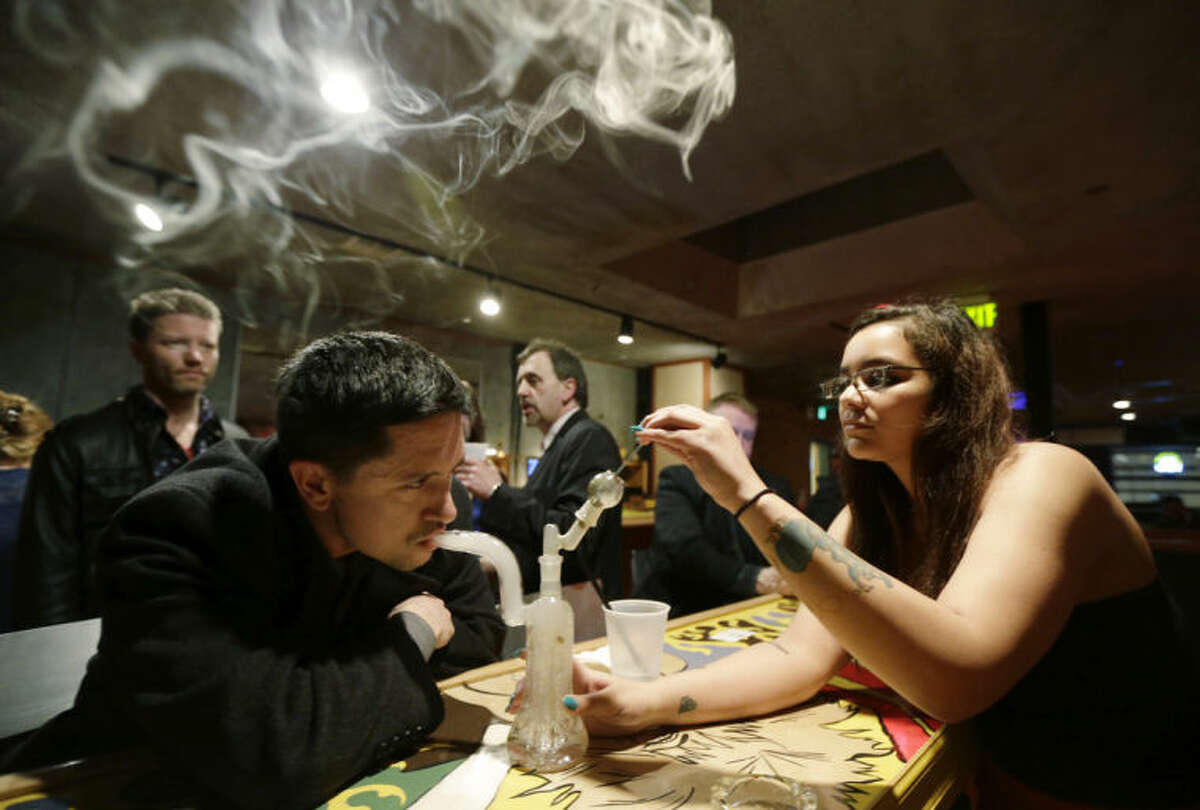 FILE - In this Saturday, March 2, 2013 file photo, John Connelly, left, inhales marijuana vapor just after midnight, with the help of bar worker Jenae DeCampo, right, in the upstairs lounge area of Stonegate, a pizza-and-rum bar in Tacoma, Wash. Owner Jeff Call charges patrons a small fee to become a member of the private second-floor club, which prohibits smoking marijuana, but does permit "vaporizing," a method that involves heating the marijuana without burning it. Washington and Colorado became the first states to pass legislation legalizing marijuana use for adults over 21. Polls show that cigarette smoking is no longer considered normal behavior, and is now less popular among teens than marijuana. (AP Photo/Ted S. Warren)
