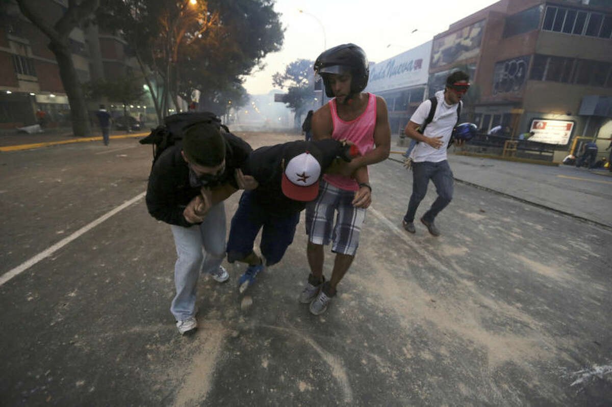 A demonstrator affected by tear gas, fired by the Bolivarian National Police, is helped after an opposition protest ended in clashes in Caracas, Venezuela, Saturday, Feb. 15, 2014. Venezuelan security forces backed by water tanks, tear gas and rubber bullets dispersed groups of anti-government demonstrators who tried to block Caracas' main highway Saturday evening. (AP Photo/Fernando Llano)