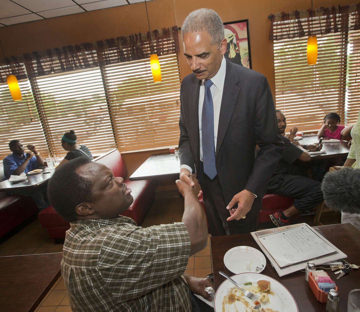 Attorney General Eric Holder stops to shake hands with a patron at Drake's Place Restaurant, before his meeting with local community leaders, Wednesday, Aug. 20, 2014 in Ferguson, Mo. Holder arrived in Missouri on Wednesday, a small group of protesters gathered outside the building where a grand jury could begin hearing evidence to determine whether a Ferguson police officer who shot 18-year-old Michael Brown should be charged in his death. (AP Photo/Pablo Martinez Monsivais, Pool)