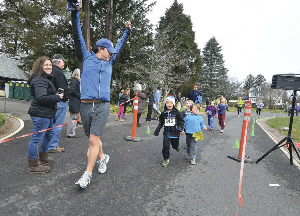 Hour Photo/Alex von Kleydorff James Knowles crosses the finish line and encourages his sons Oscar and James with him during the Rowayton Turkey Trot