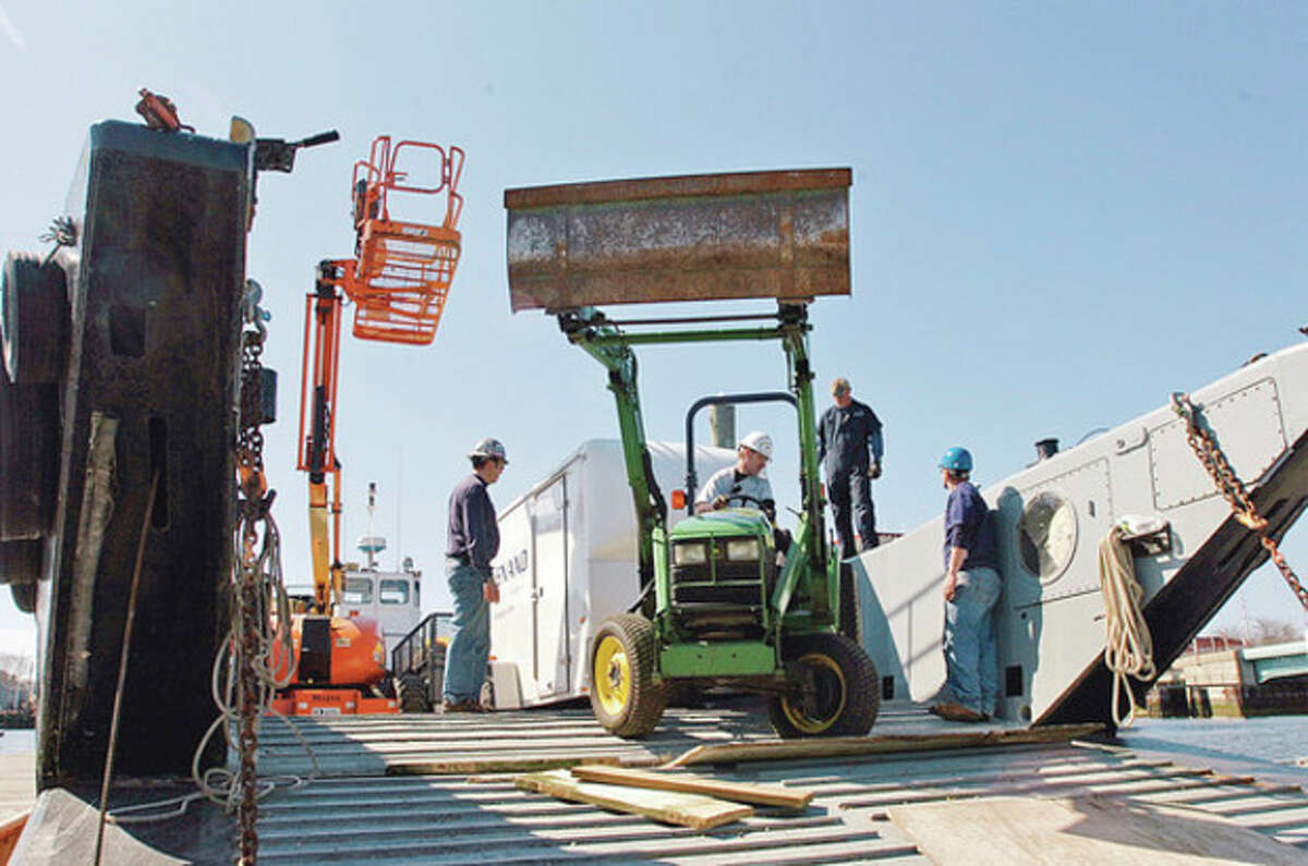 Hour photo / Erik Trautmann Workers with Cenaxo load construction equipment on a landing craft in Norwalk that will be ferried out to Sheffield Island, where restoration work on the lighthouse and outbuilding begins this week.