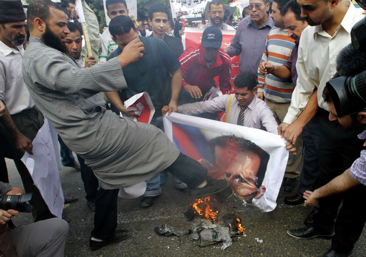 A Syrian protester kicks a burning picture of Syrian President Bashar Assad during a protest in front of the Arab League headquarters in Cairo, Egypt, Saturday, Nov.12, 2011 where an Arab League emergency session on Syria is taking place to discuss the country's failure to end bloodshed caused by government crackdowns on civil protests. Protesters called on the Arab League to suspend the country's membership. (AP Photo/Amr Nabil)