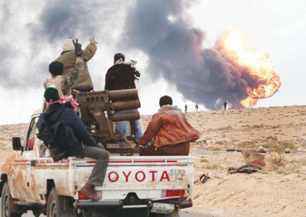 Anti-Gadhafi rebels ride on a truck with a multiple rocket launcher, as flames rises from a fuel storage facility that was attacked during fighting with pro-fighters, in Sedra, eastern Libya, Wednesday March 9, 2011. A high-ranking member of the Libyan military flew to Cairo on Wednesday with a message for Egyptian army officials from Moammar Gadhafi, whose troops pounded opposition forces with artillery barrages and gunfire in at least two major cities. Gadhafi appeared to be keeping up the momentum he has seized in recent days in his fight against rebels trying to move on the capital, Tripoli, from territory they hold in eastern Libya. (AP Photo/Hussein Malla)