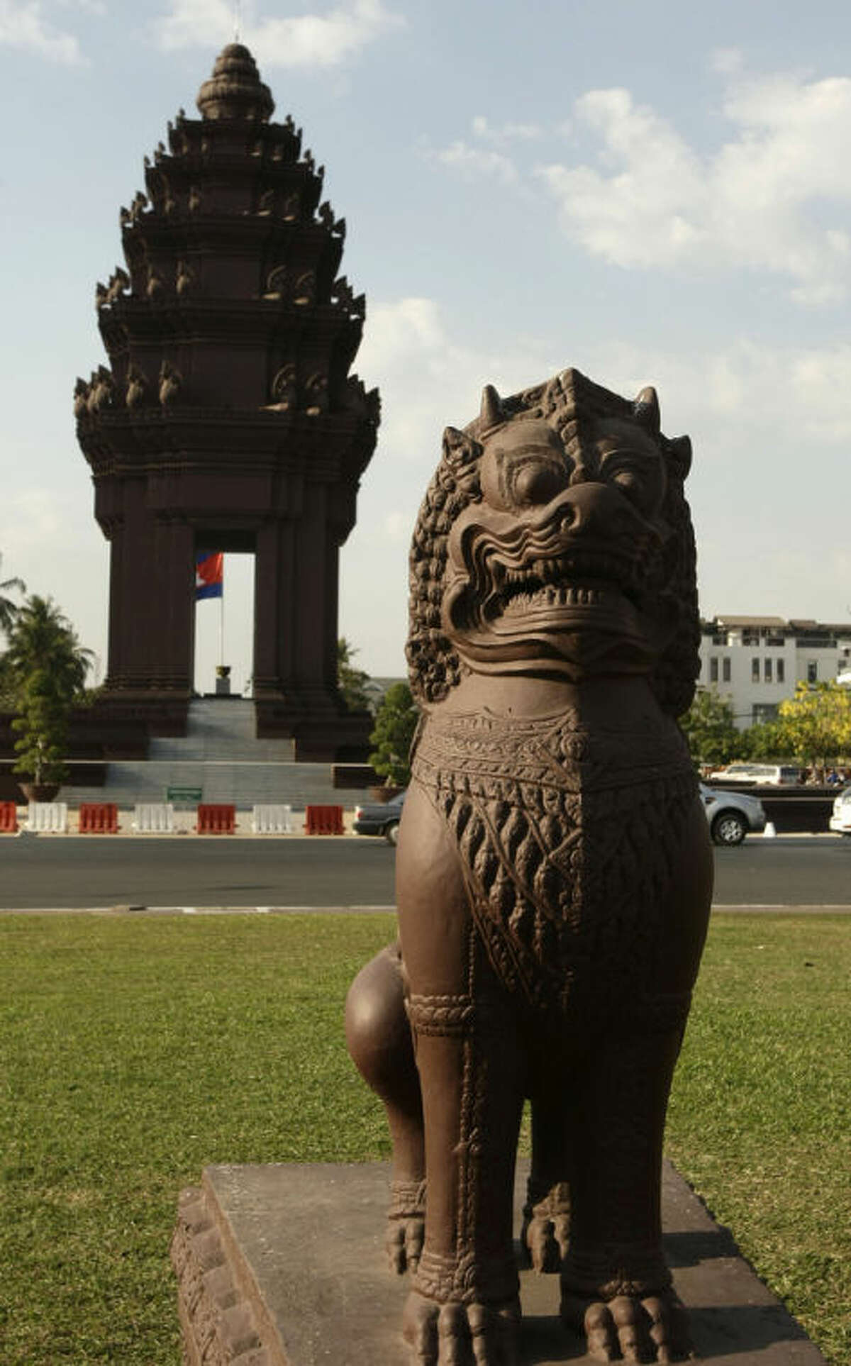In this photo taken, Feb. 25, 2013, a lion statue sits beside the Independence Monument, in Phnom Penh, Cambodia. The Independence Monument is a striking shade of terra cotta by day and brightly illuminated by night. Glowing or not, it was constructed in 1958 to commemorate independence from the French that had been achieved five years prior. (AP Photo/Heng Sinith)