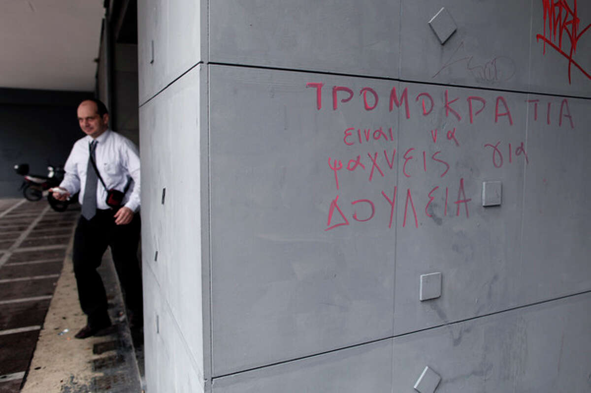 A man leaves an office of Labor Force Employment Organization (OAED) with a graffiti reading in Greek ''Terrorism = Job Seeking'' in central Athens, on Thursday, March 7, 2013. Unemployment in Greece dipped marginally to 26.4 percent in December, but experts warn that more significant improvements are unlikely in coming months. (AP Photo/Petros Giannakouris)