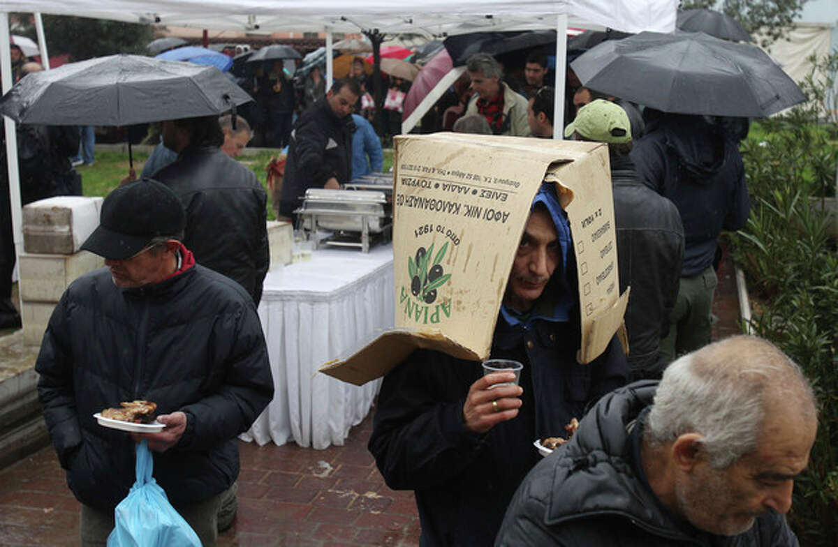A man uses a cardboard carton to protect himself from the rain as other people line up for free meat lunches under rainfall in Athens on Thursday, March 7, 2013. It's called "Barbecue Thursday" _ a raucous pre-Easter celebration for meat lovers. But this year's Tsiknopempti festivities, a fixture of the Carnival season, coincided with the Greek Statistical Authority announced unemployment in Greece has dipped marginally to 26.4 percent, according to data for December. (AP Photo/Thanassis Stavrakis)